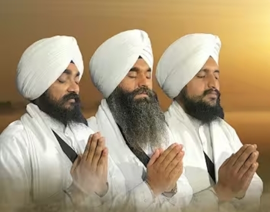 The SACVI Jatha — three Sikh musicians in white with hands folded in prayer